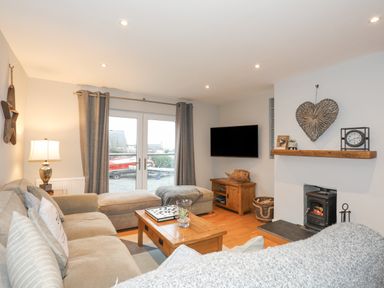A living room with a beige sofa a wooden coffee table a wall-mounted television and a fireplace at Laneton in Rhosneigr