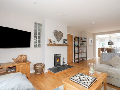 A living room with a wood burning stove a wooden coffee table and a sofa with a kitchen in the background at Laneton in Rhosneigr