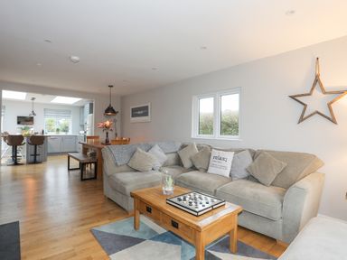 A living room with a beige sectional sofa and wooden coffee table next to an open kitchen with dining table and chairs at Laneton in Rhosneigr