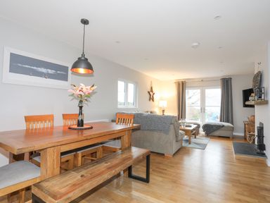 A dining area with wooden table and chairs next to a living room with sofas and a coffee table at Laneton in Rhosneigr