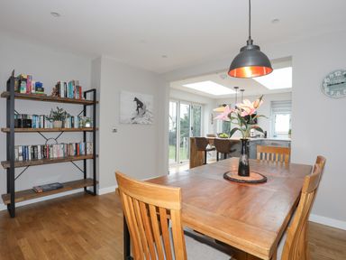 A dining room with a wooden table and chairs a bookshelf and a view of a kitchen area at Laneton in Rhosneigr