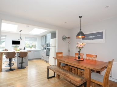 A kitchen with grey cabinets and bar stools next to a wooden dining table with chairs and a bench at Laneton in Rhosneigr