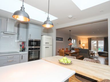 A kitchen with grey cabinets and a cream fridge next to a dining area with wooden table and chairs at Laneton in Rhosneigr