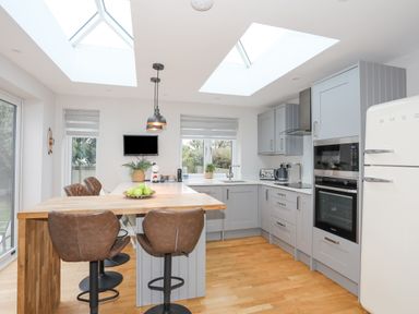 A kitchen with grey cabinets a wooden breakfast bar with stools skylights and a white fridge at Laneton in Rhosneigr