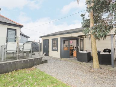 An outdoor patio area with a glass table and chairs and a small building with open doors and outdoor seating at Laneton in Rhosneigr