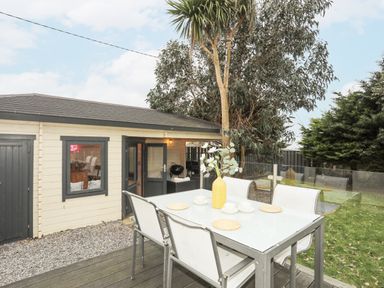 An outdoor dining area with a glass table set with cups and a yellow vase next to a small building and trees at Laneton in Rhosneigr