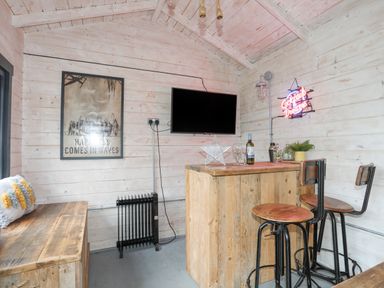 A small wooden bar area with two bar stools a wall-mounted tv and a neon sign on the wall at Laneton in Rhosneigr