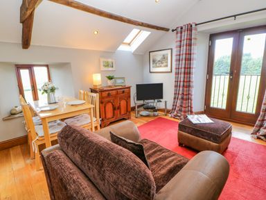 A living room with a brown sofa a wooden dining table with chairs a wooden cabinet a television and red rug at Field Barn in Alston