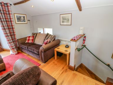 A living room with brown sofas plaid curtains a wooden side table and a staircase at Field Barn in Alston