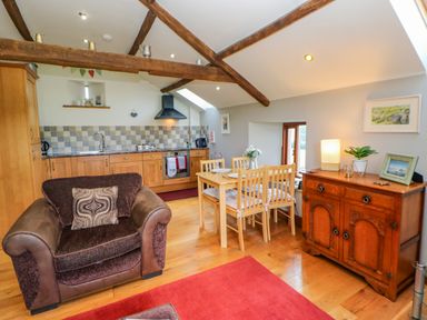 A kitchen and dining area with wooden beams wooden furniture a brown armchair and red rug at Field Barn in Alston