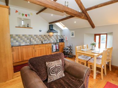 A kitchen and dining area with wooden cabinets a dining table with chairs and a brown armchair at Field Barn in Alston