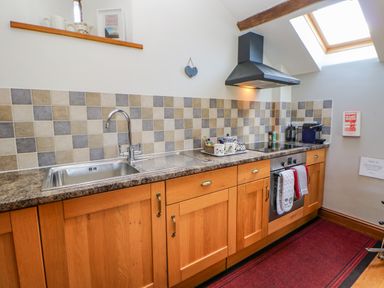 A kitchen with a stainless steel sink wooden cabinets tiled backsplash and a stove under a skylight at Field Barn in Alston