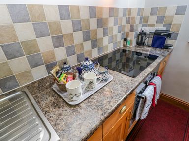 A kitchen counter with a stove sink coffee machine teapot cups and spice containers at Field Barn in Alston
