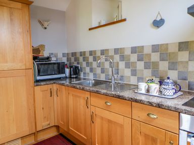 A kitchen with wooden cabinets a sink a kettle a microwave and a tray with cups and a teapot at Field Barn in Alston