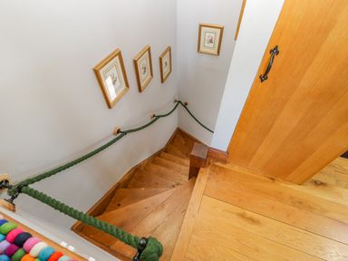 A wooden spiral staircase with green rope handrails and framed pictures on the wall at Field Barn in Alston