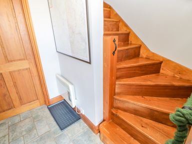 A wooden staircase with a green rope handrail next to a wooden door and a wall-mounted heater at Field Barn in Alston
