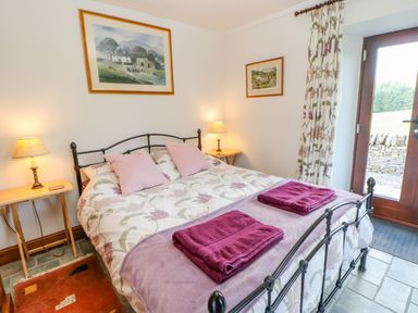 A bedroom with a bed featuring a floral comforter and purple towels with two lamps on wooden side tables at Field Barn in Alston