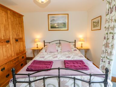 A bedroom with a double bed with pillows and folded towels bedside tables with lamps wooden wardrobe and framed pictures on the wall at Field Barn in Alston