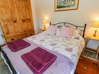A bedroom with a double bed with floral bedding and pink pillows two wooden bedside tables with lamps and a wooden wardrobe at Field Barn in Alston