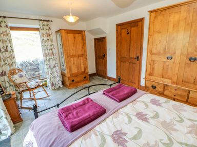 A bedroom with wooden wardrobes a rocking chair and a bed with floral bedding and folded towels at Field Barn in Alston