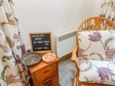 A wooden chair with floral cushions next to a wooden cabinet with metal and stone dishes and a motivational letter board at Field Barn in Alston