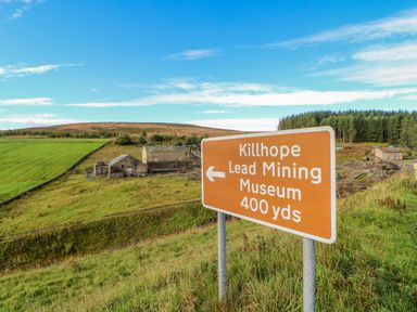 A road sign for Killhope Lead Mining Museum in a grassy rural area with buildings and trees in the background at Field Barn in Alston