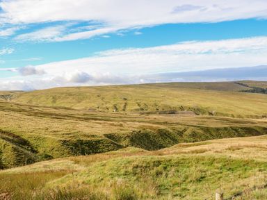 A vast grassy landscape with rolling hills under a partly cloudy sky at Field Barn in Alston