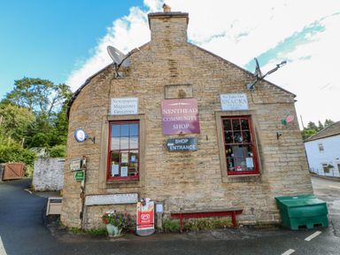 An exterior view of Nenthead Community Shop with brick walls windows and multiple signs at Nenthead