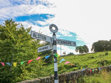 A road signpost showing directions to Alston Stanhope and Greenends with trees and grassy fields in the background at Field Barn in Alston