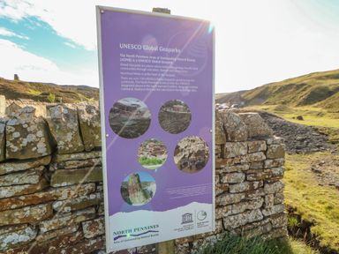 An outdoor information sign about UNESCO Global Geoparks mounted on a stone wall in a rural landscape at Field Barn in Alston