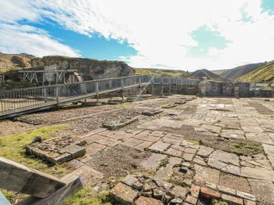 An outdoor historical site with stone ruins and a wooden walkway in a grassy hilly area at Field Barn in Alston