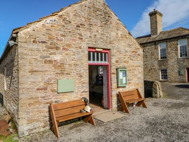 Stone building with red door and two wooden benches outside at Field Barn in Alston
