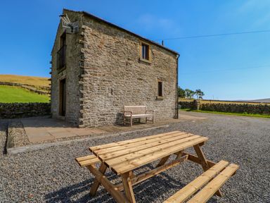A stone house with a wooden bench and picnic table outside on a gravel area at Field Barn in Alston