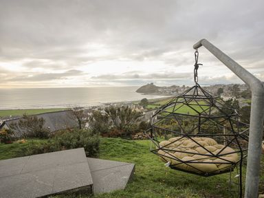 A hanging chair on a grassy hill overlooking a coastal town and the sea at Hafod Y Mor in Criccieth