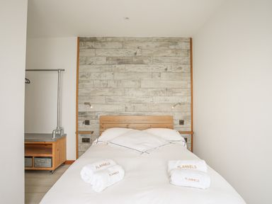 A bedroom with a bed with white linens and towels on it a wooden headboard and a wooden and metal clothes rack at Hafod Y Mor in Criccieth