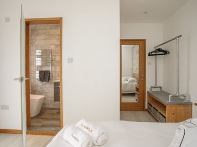 A bedroom with a bed with towels on it a door leading to a bathroom and a wooden bench with hangers at Hafod Y Mor in Criccieth