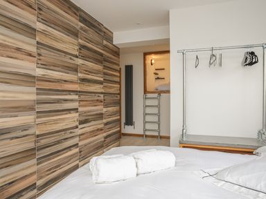 A bedroom with a bed and towels on it a wooden paneled wall and a metal hanging rack with hangers at Hafod Y Mor in Criccieth