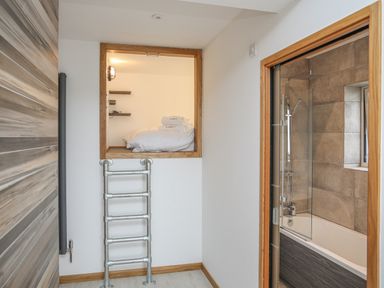 A bathroom with a bathtub and shower next to a small loft bed accessed by a metal ladder at Hafod Y Mor in Criccieth