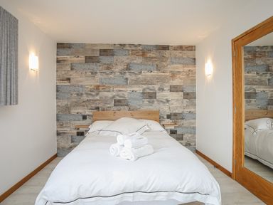 A bedroom with a bed with white linens in front of a wood paneled wall with two wall lights and a large mirror at Hafod Y Mor in Criccieth