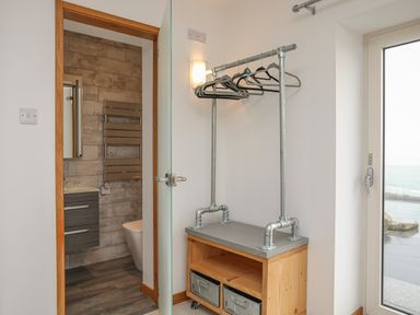 A small room with a wooden cabinet and metal hanger rack near a door leading to a bathroom at Hafod Y Mor in Criccieth