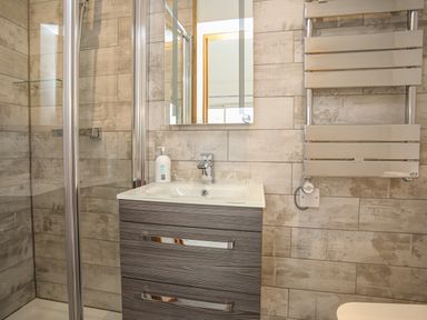 A bathroom with a shower enclosure a sink with a cabinet a wall mirror and a heated towel rail at Hafod Y Mor in Criccieth