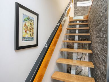 A staircase with wooden steps and a yellow handrail next to a wall with a framed picture at Hafod Y Mor in Criccieth