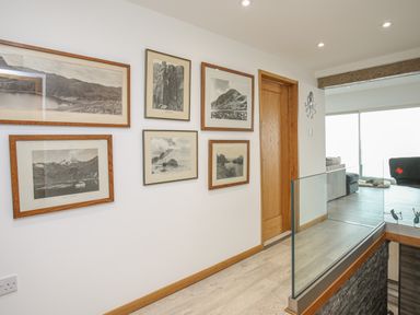 A hallway with framed pictures on the wall and a glass railing overlooking a lower level at Hafod Y Mor in Criccieth