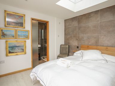 A bedroom with a bed white linens rolled towels and framed pictures on the wall at Hafod Y Mor in Criccieth