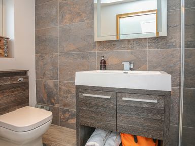 A bathroom with a toilet wooden vanity with a sink mirror and brown tiled walls at Hafod Y Mor in Criccieth