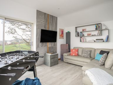 A living room with a foosball table a wall-mounted TV a sectional sofa and a bookshelf at Hafod Y Mor in Criccieth
