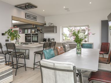 A kitchen with a dining table and colorful chairs with a vase of flowers at Hafod Y Mor in Criccieth