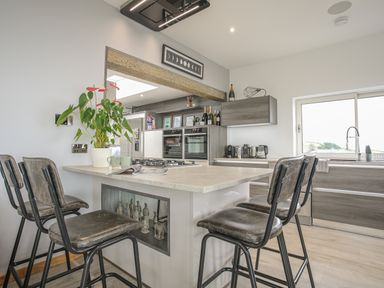 A kitchen with an island and four high chairs a plant on the island and kitchen cabinets at Hafod Y Mor in Criccieth