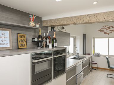 A kitchen with built-in ovens bottles on the counter and a sink by the window at Hafod Y Mor in Criccieth