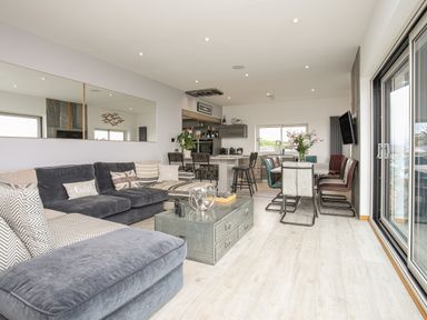 An open living room and kitchen with a large gray sectional sofa and dining table with chairs at Hafod Y Mor in Criccieth